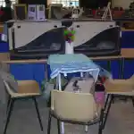 Oui mais voilà | Mes chats sont présentés dans leurs cages en tissu sur la table d’exposition lors de l’exposition féline qui s’est déroulée à Troyes dans l’Aube. Cette photo a été prise le matin, lors de l’entrée des exposants. Une autre table est positionnée devant, avec des chaises pour nous asseoir tout au long de cette journée. Sur cette table, des plumeaux colorés sont disposés au centre.