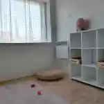 La vision de notre élevage, l'espace de mes chats | Montre l’intérieur lumineux et minimaliste de la pièce dédiée à mes chats. L’espace comprend une étagère en bois de 6 cases de couleur blanche sur laquelle est posée une lampe à sel d’Himalaya. Un tapis rose est posé sur le sol où traînent des jouets pour chats. Un pouf, tressé à la main en fibres de bananier, qui sert indifféremment de couchage et de griffoir pour mes chats, est visible en face, légèrement sur la droite en regardant la photo.